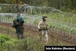 Латвійський прикордонник і військовослужбовець проходять повз тимчасову огорожу з колючого дроту на латвійсько-білоруському кордоні поблизу Робежнієкі (Латвія), 28 вересня 2021 року