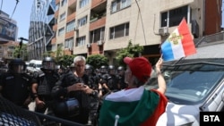  Протестиращ развява знаме пред чиновници на полицията, отделили достъпа до постройката на Европейска комисия в София. 