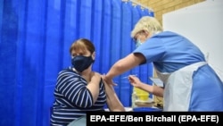 Egy nő az első adag oltást kapja a Pfizer–BioNTech-vakcinából egy cardiffi oltóponton 2020. december 8-án