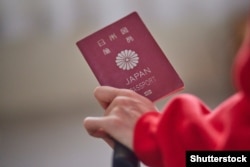 A woman holds a passport featuring the imperial crest of Japan.