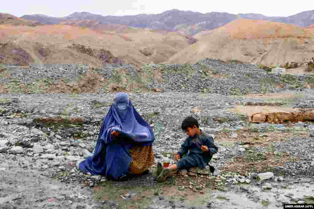 A burqa-clad Afghan woman looking for alms sits beside a child along a street on the outskirts of Fayzabad district in Badakhshan Province.