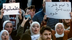 Femei siriene scandând sloganuri și ținând în mâini pancarte în limba arabă pe care scrie: „Nu există societate liberă fără femei libere” (dreapta) și „Secularism” (stânga), la o manifestație de revendicare a unui stat secular, Damasc, Siria, 19 decembrie 2024.