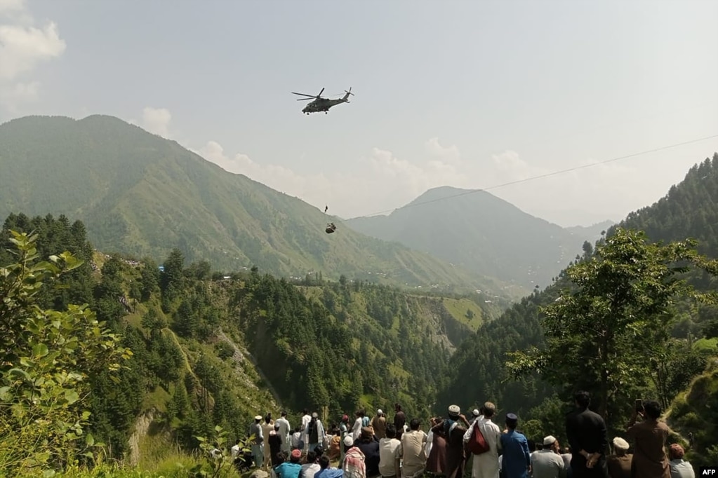 Njerëzit shikojnë se si një ushtar zbret nga një helikopter gjatë një misioni për të shpëtuar studentët e ngecur në një gondolë në fshatin Pashto në provincën malore Kyber Pakhtunkva më 22 gusht. Të tetë personat u shpëtuan përfundimisht.