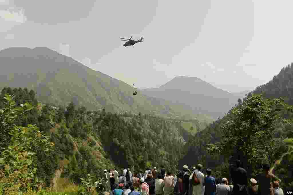 Njerëzit shikojnë se si një ushtar zbret nga një helikopter gjatë një misioni për të shpëtuar studentët e ngecur në një gondolë në fshatin Pashto në provincën malore Kyber Pakhtunkva më 22 gusht. Të tetë personat u shpëtuan përfundimisht.