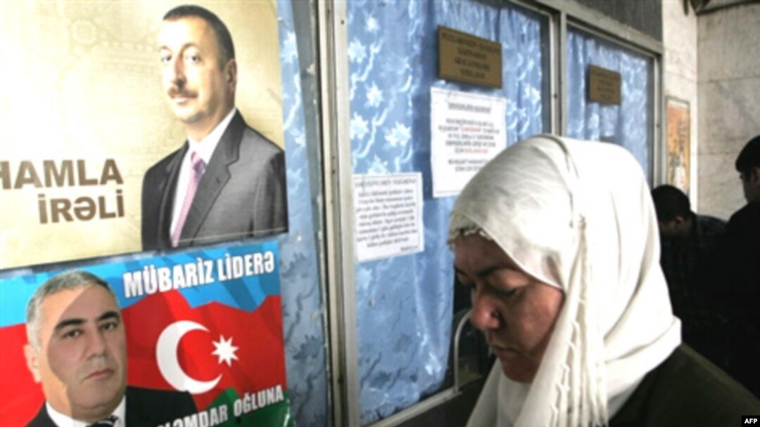 A woman stands near election posters for current Azerbaijani President Ilham Aliyev 