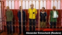 Left to right: Andrew Hill (Britain), Dylan Healy (Britain), Vjekoslav Prebeg (Croatia), John Harding (Britain), and Mathias Gustafsson (Sweden), stand in a defendants' cage as they attend a court hearing in Donetsk, Ukraine, on August 15, 2022.