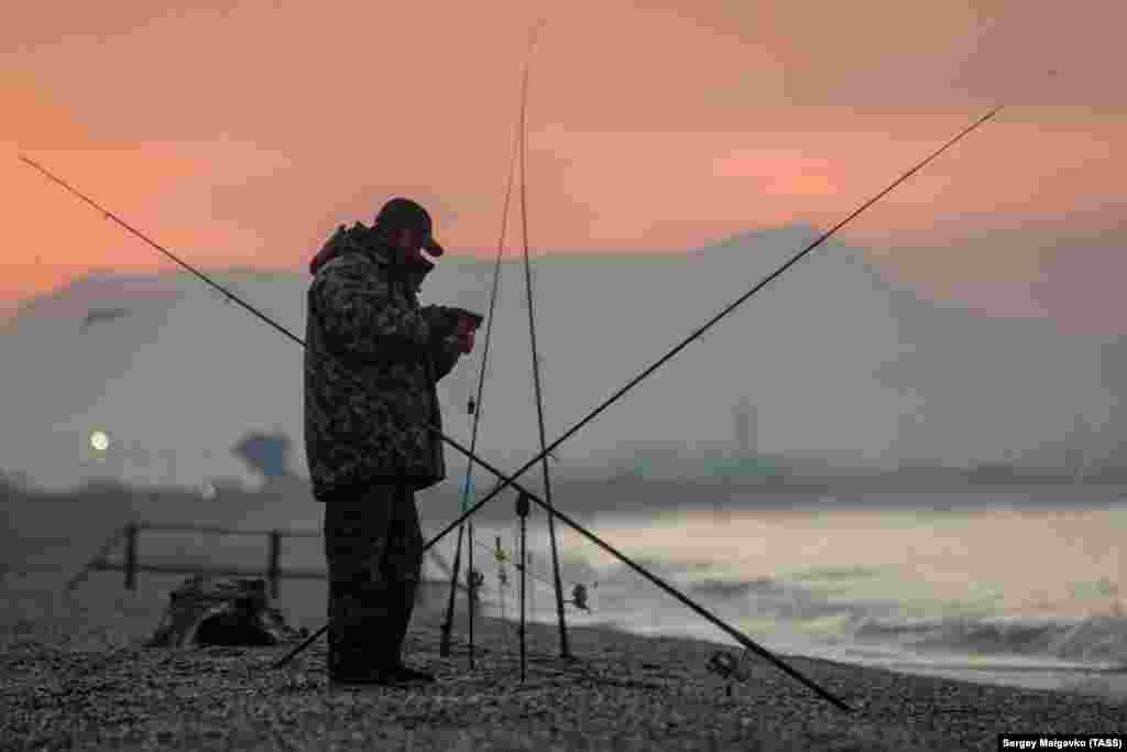Огненный закат солнца и рыбак на берегу Черного моря в окрестностях Сак, декабрь 2020 года