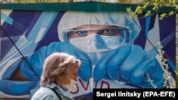 Жінка в захисній масці на тлі плакату з зображенням лікаря, Московська область, Росія, травень 2020 року