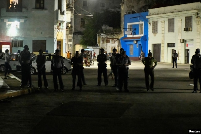 Кубинские полицейские наблюдают за протестующими против очередного отключения электричества. Гавана, 21 октября 2024 года