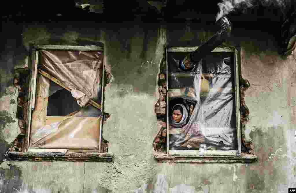 A Syrian refugee woman looks out from a window with no glass in a house in the Kucukpazar area of Istanbul, Turkey. (AFP/Gurcan Ozturk)