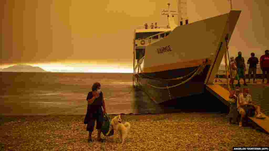 Egy nő várja a kutyájával együtt a kompot, hogy elhagyja otthonát Evia szigetén.