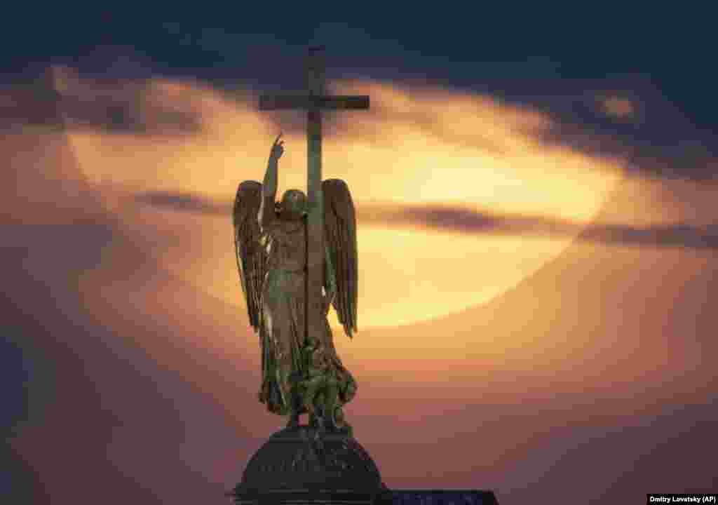 A full moon rises over a statue of an angel fixed atop the Aleksandr Column in Palace Square in St. Petersburg, Russia.