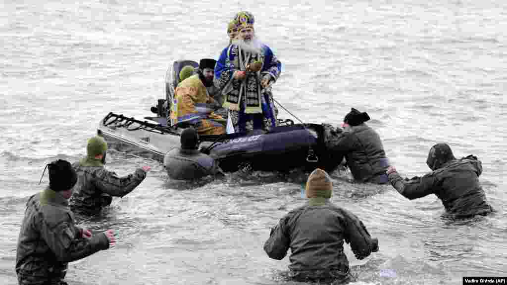 Military divers walk to a boat carrying Archbishop Teodosie, a Romanian cleric, during an Epiphany service in Constanta, Romania. (AP/Vadim Ghirda)