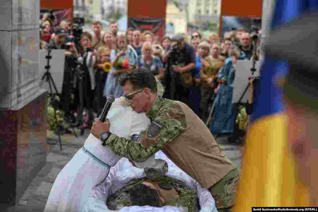 Дружина Олексія Євгенія та його побратим із команди пошуковців над труною Олексія у Києві на Майдані Незалежності під час прощання з Олексієм, 8 серпня 2026 року