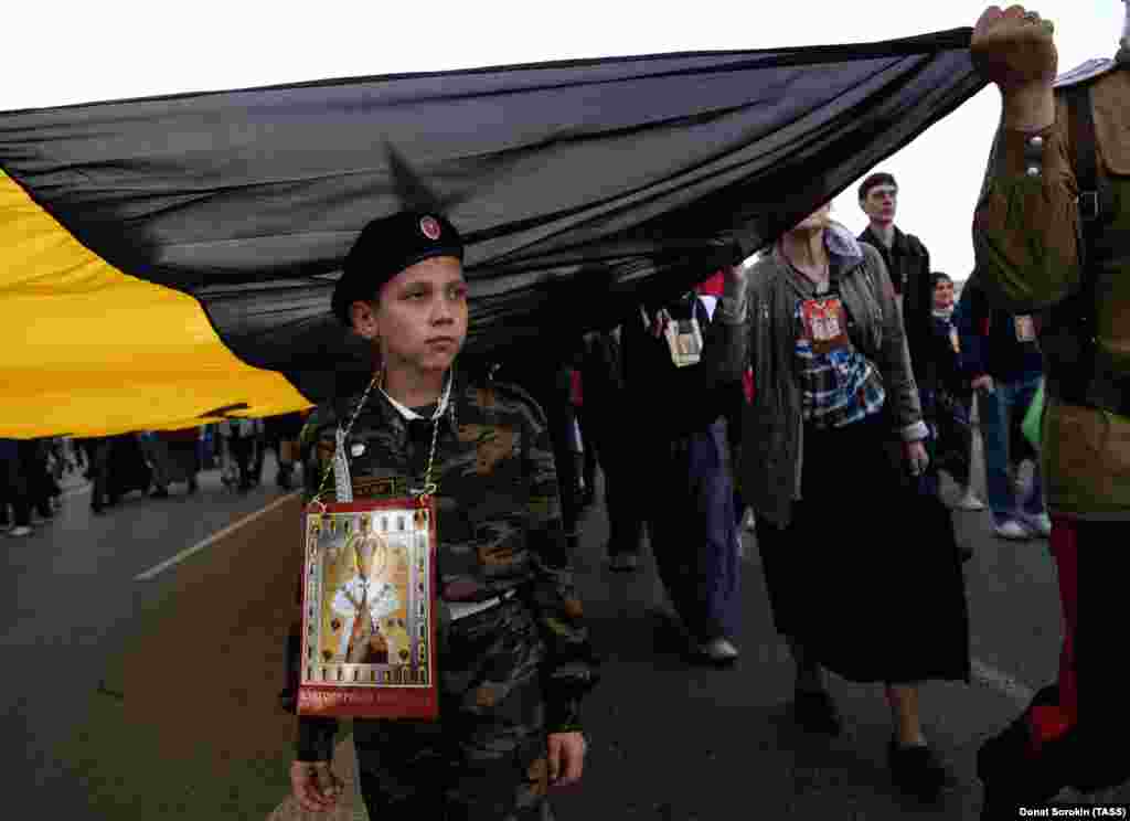 A boy walks beneath the yellow, black, and white flag of Imperial Russia.&nbsp;