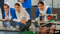 Afghan all-girls robotics team, with their robot nearby, watch other country's robots in Washington D.C.