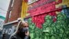 RUSSIA -- A woman wearing a protective mask walks in front of a graffiti showing a coronavirus related scene on a wall in Moscow, January 26, 2021