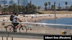 Велосипедист в маске проезжает мимо пляжа в Барселоне, Испания. 30 июля 2020 года.