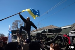 Особи, що штурмують частину морської авіації в Новофедорівці, зривають український прапор, Крим, 22 березня 2014 року