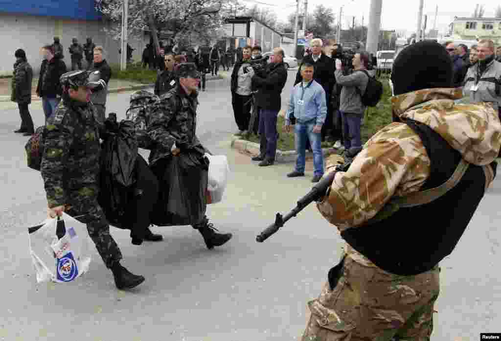 Ukraine -- Ukrainian servicemen carry their belongings as they pass by an armed man while leaving the territory of the naval headquarters in Sevastopol, March 19, 2014