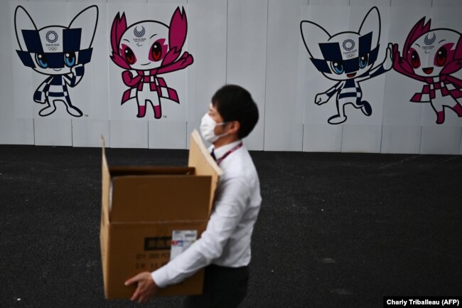 Владелец закрывающегося магазина в Токио на фоне уличной рекламы отложенной Олимпиады-2020. 17 апреля 2020 года