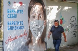 Ер кісі маска таққан әйел бейнеленген баннердің жанынан өтіп барады. Алматы, 11 қыркүйек 2020 жыл.