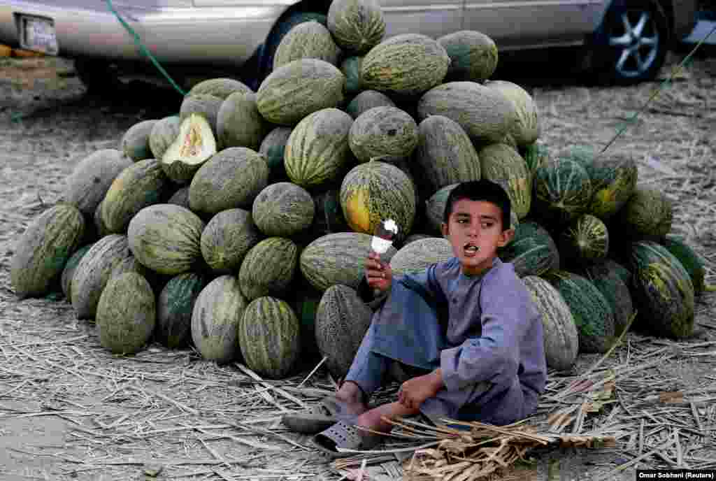 An Afghan boy enjoys an ice cream as he sells melons at a market in Kabul. (Reuters/Omar Sobhani)