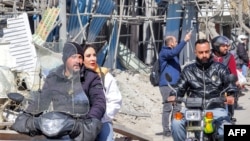 عبور مردم از کنار ساختمان‌های ویران‌شده در حملات هوایی در نزدیکی میدان فردوسی تهران، ۱۲ اسفند