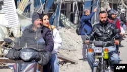 Хора карат мотоциклети край разрушени сгради в центъра на Техеран, 3 март 2026 г.