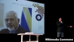 Wikipedia Senior Manager Arash Soleimani giving a speech at the 14th anniversary of Persian Wikipedia next to the image of Javad Zarif.December 2017