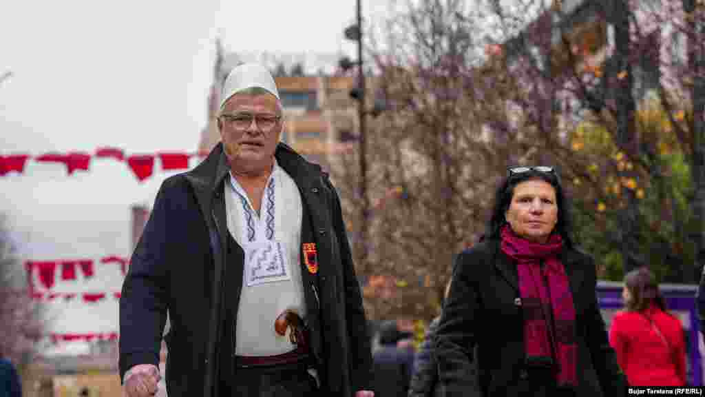 Një burrë me plis në kokë, emblemë të UÇK-së dhe kobure në brez.