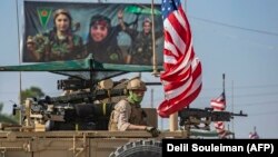 FILE: A U.S. armored vehicle drives past a billboard for the Syrian Kurdish Women's Protection Units (YPJ), during a patrol of the Syrian northeastern town of Qahtaniyah at the border with Turkey, in October.