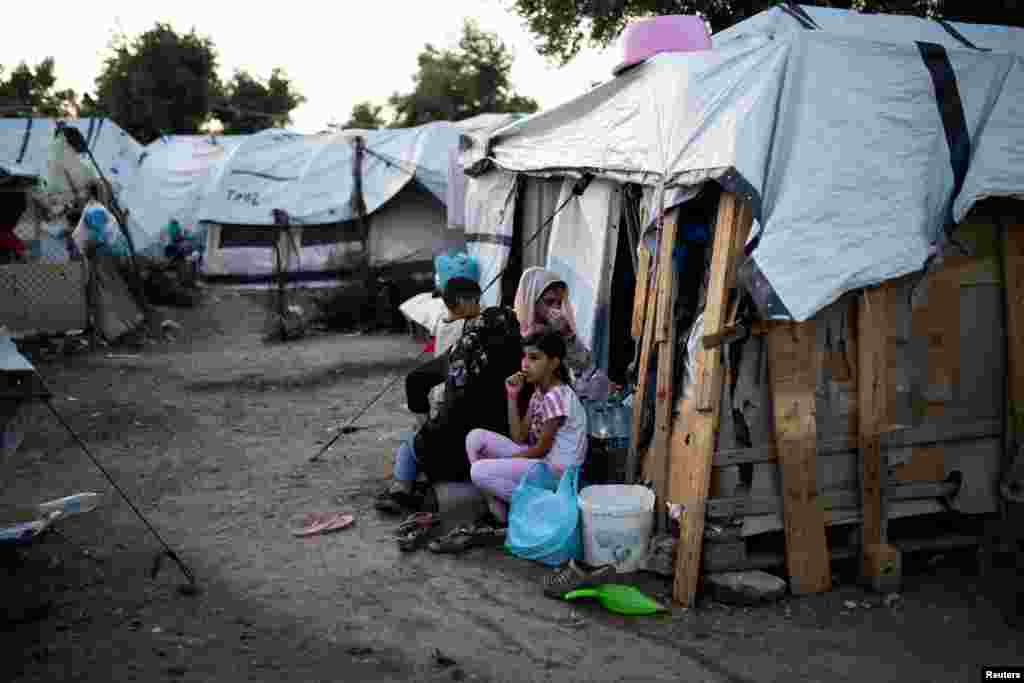 Migrantët tjerë qëndrojnë jashtë tendës së tyre në një kamp të improvizuar.