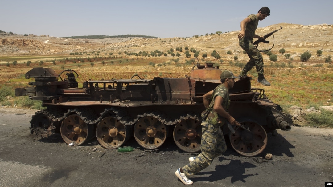 Syrian rebel fighters are pictured next to a burnt-out army tank in the northern town of Atareb, 25 kilometers east of Syria's largest city, Aleppo, on July 31.