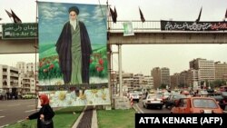 An Iranian woman passes a huge portrait of late Ayatollah Khomeini, 07 June, 1999 in Tehran, as Iran commemorates the tenth anniversary of the Ayatollah's death.