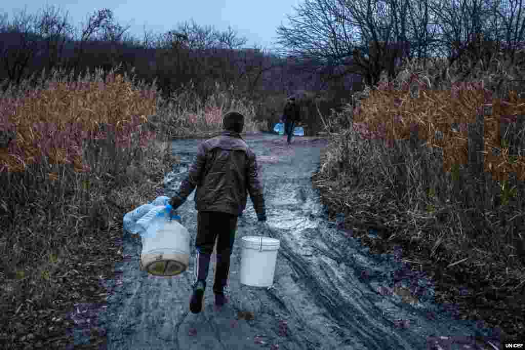 23-річний Іван несе порожні бутилі, щоб набрати води для своєї сім&rsquo;ї, у якій дев&rsquo;ятеро братів і сестер. Сім&rsquo;я живе у Торецьку на Донеччині. Тут часто трапляються тривалі перебої з водопостачанням через пошкодження водопроводу внаслідок обстрілів. Навіть у ті короткі періоди, коли вода є, сім&rsquo;ї її не вистачає. Тому питну воду беруть із місцевого джерела. У місяці, коли вода була повністю відключена, у черзі до джерела люди стояли довгі години.