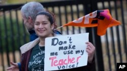 Câțiva profesori țin steaguri și pancarte de protest în fața școlii Holland Park, în timpul grevei cauzate de salariile prea mici, Londra, miercuri, 1 februarie 2023. 