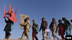 FILE: Afghan refugees, who have voluntarily returned from neighboring Pakistan with assistance from United Nation High Commissioner for Refugees (UNHCR) carry a chair and a board to attend an open air school outside their temporary shelters in the eastern Nangarhar Province.