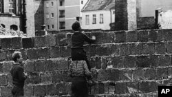 A boy sitting on the shoulders of another child peers over the wall on Liesen Street in West Berlinon August 23, 1961.