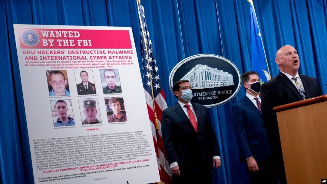 Издөөгө алынган орус хакерлеринин сүрөттөрү бар көрнөктүн жанында Федералдык иликтөө бюросунун (ФИБ) өкүлү Майкл Кристман (оңдо), Улуттук коопсуздук бөлүмүнүн өкүлү Жон Демерс (солдо) жана ФИБдин директорунун орун басары Дэвид Боудич турат. Вашингтон. 2020-жылдын 19-октябры. 