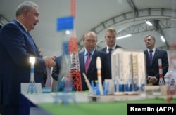 Președintele rus Vladimir Putin (centru) ascultă explicațiile șefului de-atunci al agenției spațiale ruse Roskosmos, Dmitri Rogozin (stânga), în timp ce vizitează cosmodromul Vostocini, în septembrie 2021.
