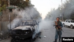 An Afghan policeman patrols next to a burning vehicle in Kunduz on October 1.