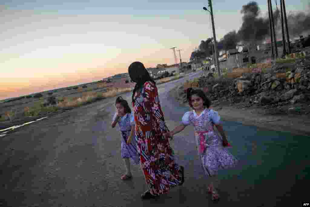 Girls walk with their mother as she turns to look at smoke billowing from three shells dropped on the town of Al-Bara in the northwestern Syrian province of Idlib. (AFP/Daniel Leal-Olivas)