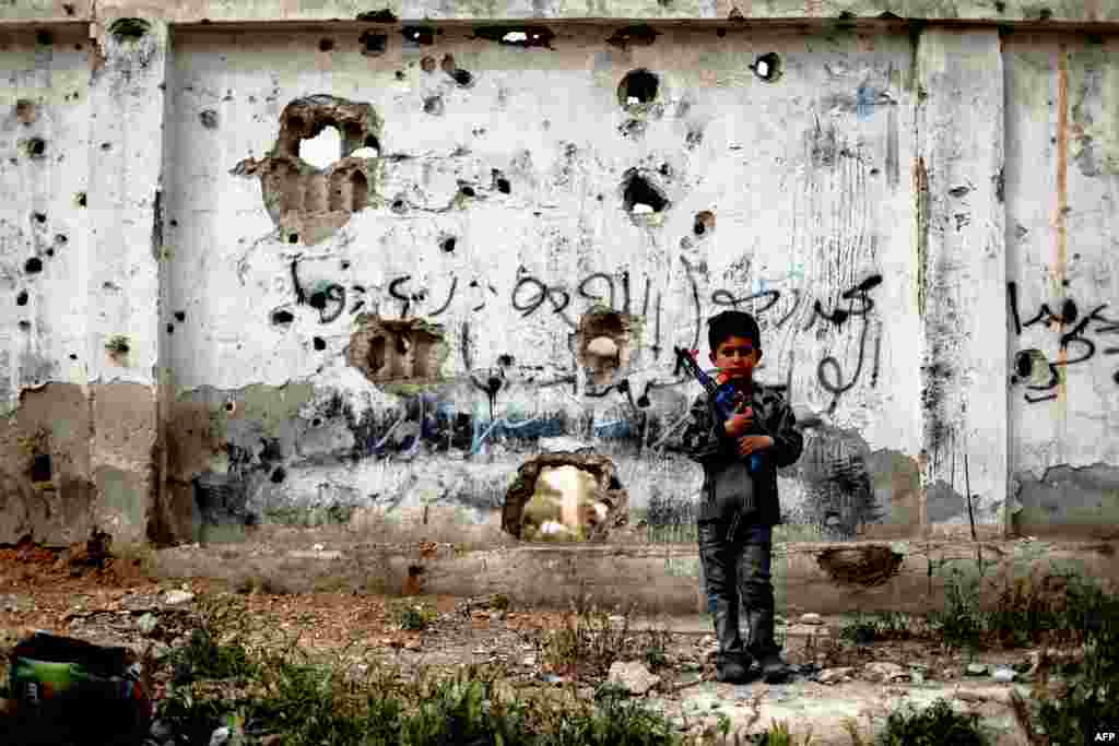 A Syrian boy stands with a toy gun in front of a bullet-riddled wall in the rebel-held town of Douma, on the eastern outskirts of the Syrian capital, Damascus. (AFP/Sameer al-Doumy)