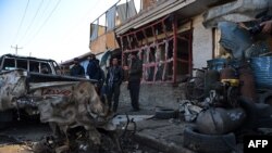 Afghan onlookers stand at the site of a suicide car bomb near the international airport in Kabul on December 28, 2015.