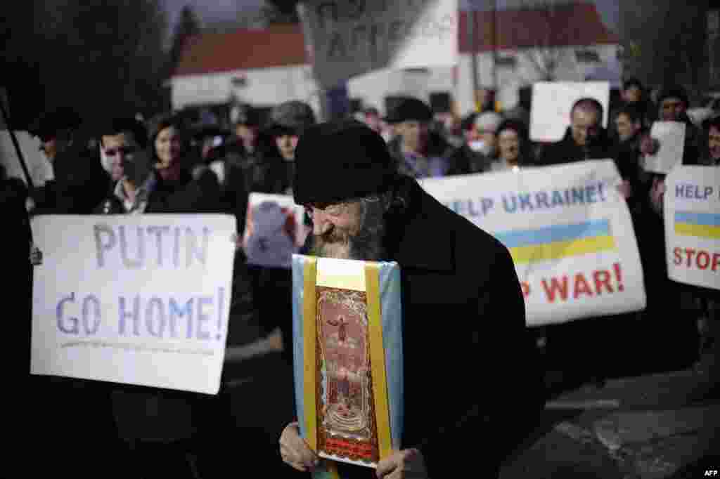 A monk carries an icon and demonstrators hold placards reading, &quot;Putin go home!&quot; and &quot;Help Ukraine! Stop war!&quot; during an antiwar rally in front of the Russian Embassy in Kyiv on March 7. (AFP/Dimitar Dilkoff)