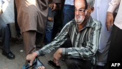 A cobbler wearing a mask of British author Salman Rushdie polishes shoes outside a mosque during a protest by an Islamic organization in Mumbai on January 11, ahead of the planned visit.