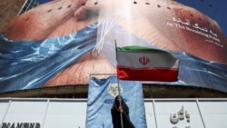 A woman holds an Iranian flag in Tehran on May 25 near an anti-American billboard depicting US President Donald Trump and the Strait of Hormuz.