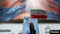 Një grua mban një flamur iranian në Teheran më 25 maj pranë një billboardi anti-amerikan që përshkruan presidentin e SHBA-së, Donald Trump, dhe Ngushticën e Hormuzit.