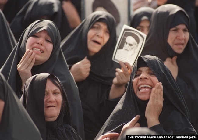 Women brandish an Ayatollah Khomeiny's portrait as hundreds of thousands of Iranians gather to catch a glimpse of the Iranian spiritual leader in a glass coffin at the Mossala prayer ground in northeastern Tehran 05 June 1989.